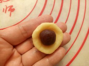 取一个面团按扁放入一个豆沙馅包好，收口捏紧。