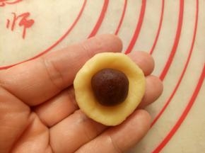 取一个面团按扁放入一个豆沙馅包好，收口捏紧。