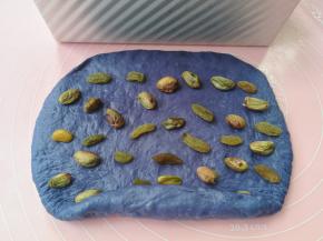 面团松弛好之后，先取小份的蓝色面团擀开成长方形，长度比吐司盒略短一点，翻面使光滑面向下，然后在上面撒葡萄干和开心果（这份是不需要放无花果干的）