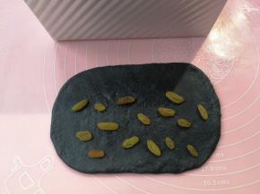 然后来处理黑色面团，同样擀开呈长度比吐司盒略短的方形，翻面后撒一点葡萄干即可