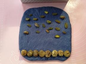 大份的蓝色面团同样擀开翻面，然后在卷起的头部位置摆上一排无花果干，在尾部再撒少量的葡萄干和开心果，收口位置不撒干果
