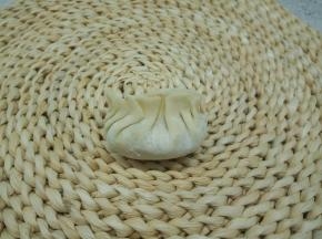 在饺子皮放适量的馅，饺子皮四周沾上水，使皮容易粘合，饺子皮中间先捏一下，两边向中间将饺子皮边缘弄成褶皱状，