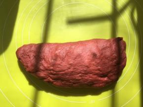 将红色面团取出，在揉面垫上按压排气