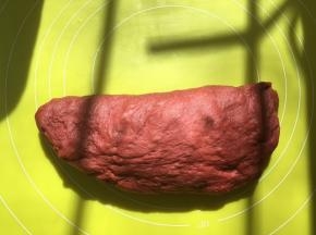 将红色面团取出，在揉面垫上按压排气