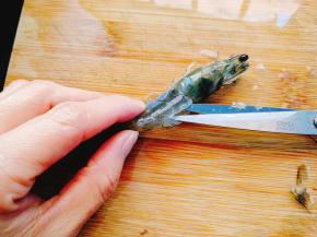 然后，用剪刀对准虾头和虾身的交界处，将这个地方剪断多一半，留下一小半连接头身，沿着虾背的背脊线剪开。不但要剪开虾壳，还要剪开三分之二厚度的虾肉，留下三分之一来连接保持虾肉不会散开。