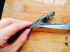然后，用剪刀对准虾头和虾身的交界处，将这个地方剪断多一半，留下一小半连接头身，沿着虾背的背脊线剪开。不但要剪开虾壳，还要剪开三分之二厚度的虾肉，留下三分之一来连接保持虾肉不会散开。