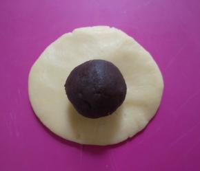 冷藏好的面团分成30克一份。取一面团按扁，包入一个豆沙馅。