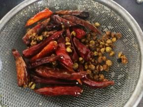 把花椒和尖辣椒用滤网沥下油，尖辣椒和花椒倒了