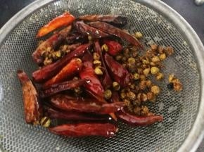 把花椒和尖辣椒用滤网沥下油，尖辣椒和花椒倒了