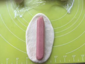 取一根香肠，放在擀好的面皮中间，用面皮包裹上香肠，捏紧收口
