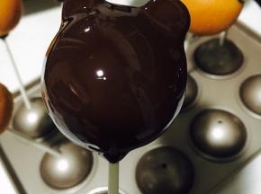 把黑巧克力液淋满整个棒棒糖。「棒棒糖头朝下垂直一会，可以过滤下多余的巧克力液，使其表面更光滑，不会从纸棒流下。」