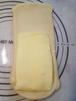 把醒好的面团根据擀成比黄油片稍宽一点，长约1.5倍的长方片状，将黄油片摆在2/3处。