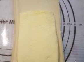 把醒好的面团根据擀成比黄油片稍宽一点，长约1.5倍的长方片状，将黄油片摆在2/3处。