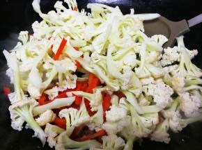倒入花菜和红辣椒，翻炒均匀后加一点清水，翻炒两分钟左右