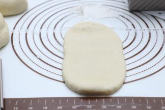 取出发酵好的面团进行排气，分隔成两个吐司盒用量（450g+水立方吐司盒一个用量）排气后擀至长舌状后从一端卷至另一端。