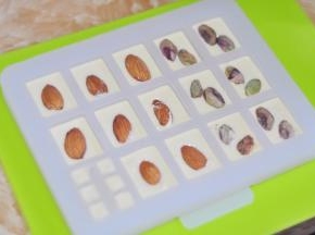 将白巧克力用勺子舀入到模具中，填至六分满，然后拿起案板，从半空中平摔几下，让震出里面的空气。放入果仁，轻轻按压一下。放入冰箱冷藏一会，让巧克力凝固。