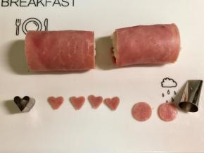在另一片火腿片上，用心形模具切下4个爱心形做小猪的耳朵。用裱花嘴圆形的一端切下两个圆形做小猪的鼻子。