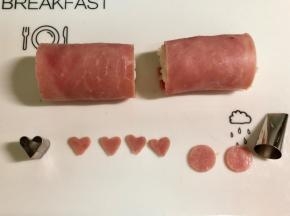 在另一片火腿片上，用心形模具切下4个爱心形做小猪的耳朵。用裱花嘴圆形的一端切下两个圆形做小猪的鼻子。