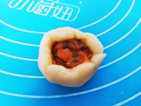 取一份面团压扁，上面放一点咸蛋黄肉松馅，收口处捏紧，搓圆