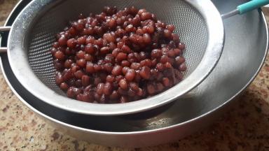 加入170克老冰糖，一直煮至红小豆开花水也基本煮干为止，把煮好的红小豆放在筛上空干，去除多余的水分。