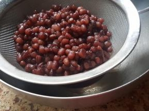加入170克老冰糖，一直煮至红小豆开花水也基本煮干为止，把煮好的红小豆放在筛上空干，去除多余的水分。