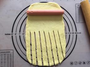 拿出一个面团擀成长方形，将火腿肠放在上面，下面用刀划出条状