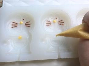 黄色巧克力融化后装入裱花袋，剪个小口，挤入鼻子和项圈和铃铛处