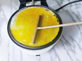 待面糊表面凝固后，将鸡蛋直接敲在煎饼上面，继续摊均匀。