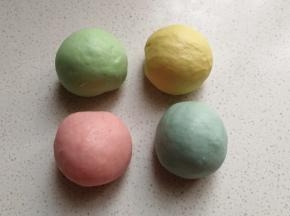 四份小面团中分别加入四种颜色的食用色素，揉均匀后并滚圆，再摆入烤盘中盖上保鲜膜放温暖处发酵