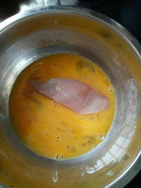 把一块鸡肉放入蛋黄液中裹上蛋液。