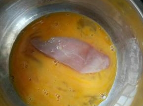 把一块鸡肉放入蛋黄液中裹上蛋液。
