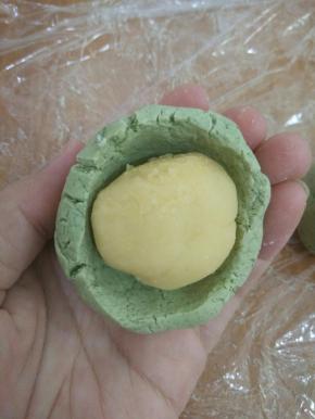 取个艾叶面团，用拇指在中间慢慢转出一个洞，放入绿豆馅。