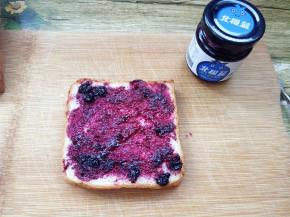 取一片面包片，用抹刀在面包片表面抹一层蓝莓酱，看，有大颗的蓝莓果肉呦；