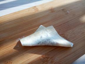 取一张馄饨皮，加少许肉馅，斜角对折（对折处可以沾点水，粘合起来容易）