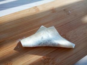 取一张馄饨皮，加少许肉馅，斜角对折（对折处可以沾点水，粘合起来容易）