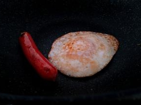 在把鸡蛋和热狗肠煎熟。