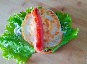 饼上面铺上生菜，涂上沙拉酱，放上鸡蛋和热狗肠。