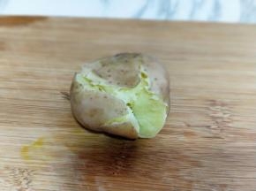 将煮熟的小土豆放在砧板上，用刀身轻轻的压一下，不用压的太扁，边缘稍微裂开一点即可。