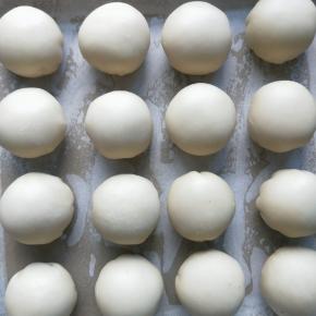 把擀好之后的油酥皮，每一个都包上豆沙蛋黄馅，收口朝下，依次放在铺满油纸的烤盘上。