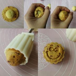 将蔓越莓面团的小剂子压扁放上绿豆沙，利用虎口将面团边缘慢慢往上推，把豆沙包入后收圆，如意坊的表情包模具装入喜欢的花片后，在模具内壁和花片上撒适量手粉防粘，抖去多余手粉后，将包好的南瓜饼坯放入模具桶身，垂直放置好模具后轻压到底，然后拎起模具的同时慢慢推出印好的南瓜饼坯～哇！是个阳光灿烂的大笑脸哦～