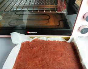揭去上面一层油纸，把擀好的肉脯放入烤盘里。