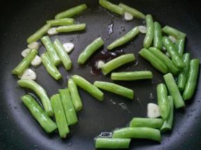 将四季豆炒熟至七成熟，放入蒜瓣，煸炒出香味。