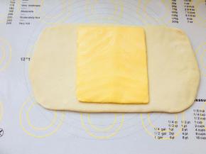 面团冷冻结束的前15分钟，将黄油片从冰箱拿出回温。黄油不可太硬，要可以轻轻弯曲，手按有轻微手痕为宜。将面团擀成长方形，大小可以包裹住黄油片即可。将黄油片放置到面片上时，轻轻按压黄油片，让它与面团更紧密。