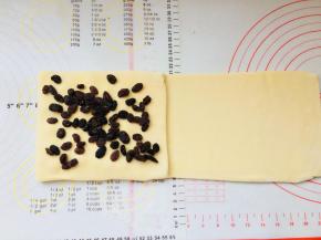 掀起左侧三分之一折向右侧，盖住之前中间位置的葡萄干。再放置葡萄干与这层上。