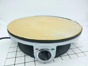 煎饼机插好电源，拧开、再预热煎饼机2分钟，舀一勺面糊倒入煎饼机中间，用木推将中间的面糊往四周摊开