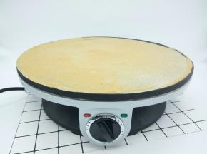 煎饼机插好电源，拧开、再预热煎饼机2分钟，舀一勺面糊倒入煎饼机中间，用木推将中间的面糊往四周摊开