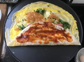 这时，将煎饼的一边对折一下，抹上蒜蓉甜面酱。