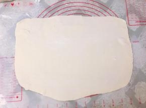 硅胶垫上撒上少许面粉，取一个剂子擀成大长方形薄片。