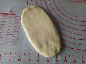 取一个面团按扁，用擀面杖擀成椭圆形，大小根据烤肠的大小来
