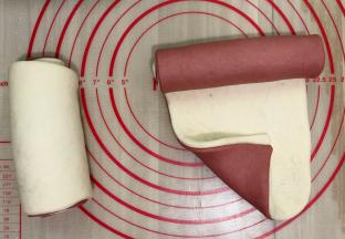 我把两个颜色一分为二，一个用红色的面皮在下，一个用白色面皮在下，这样两个卷出来的花色就不一样了，这个可按个人喜好，将两块面团重叠起来，用擀面杖轻轻按压，擀平，使两块面皮完全重叠。在重叠的面皮上抹上一点点水，尽量的抹均匀一点，这一步是不可以忽略的，至于重叠顺序没有规定。